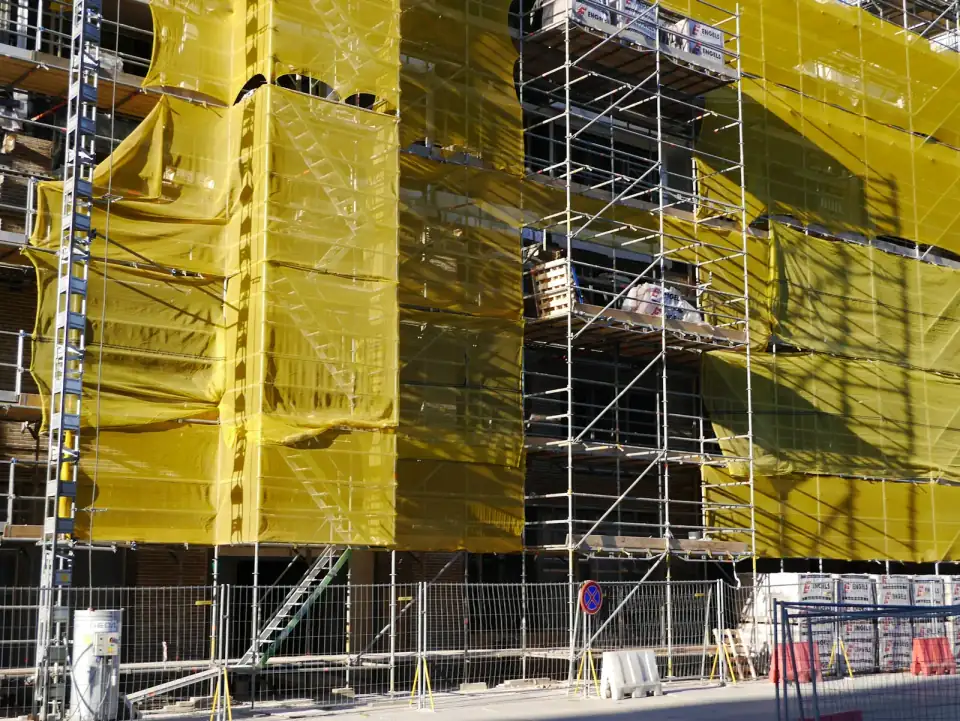 Steigers met geel bouwdoek rond nieuwe woningen in aanbouw in Amsterdam